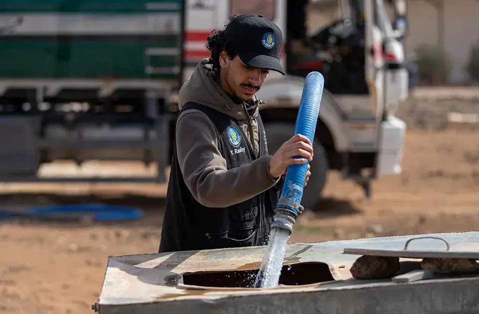 An HDF water technician filling a family's tank with clean water in a camp in Jordan