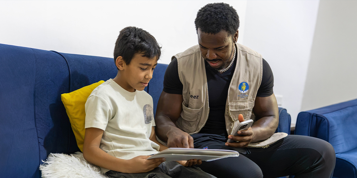 An HDF field worker sitting with a boy in Jordan, reading together